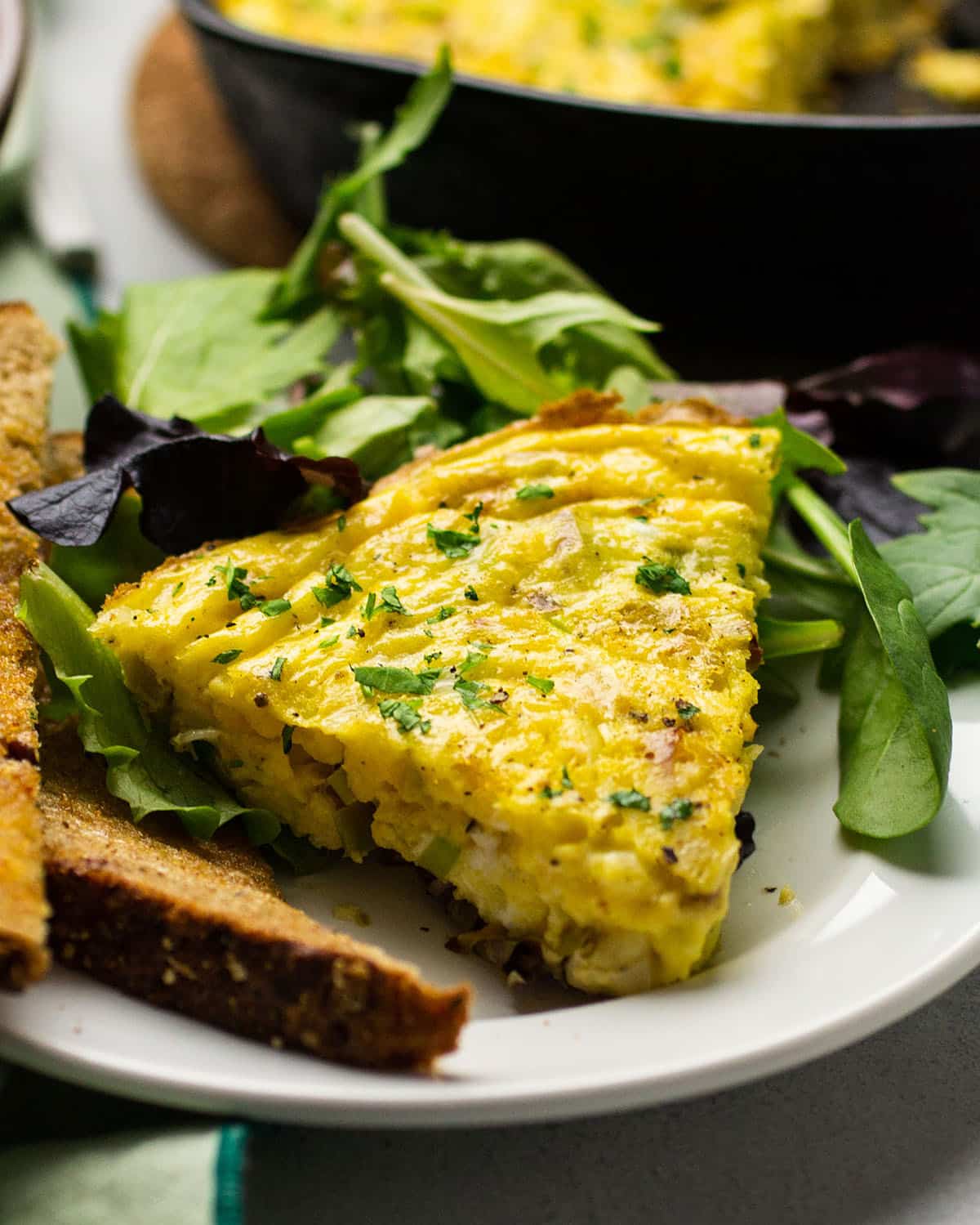 Slice of leek frittata on a plate with salad.