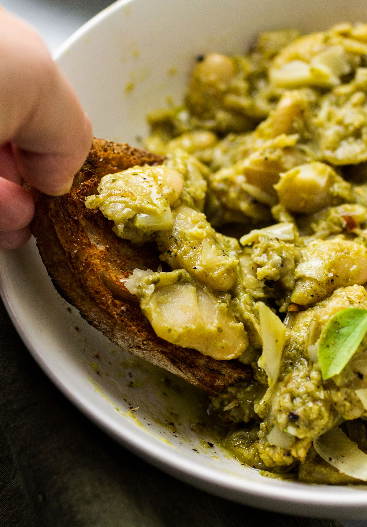 Dipping a slice of toasted bread into a bowl of pesto beans.