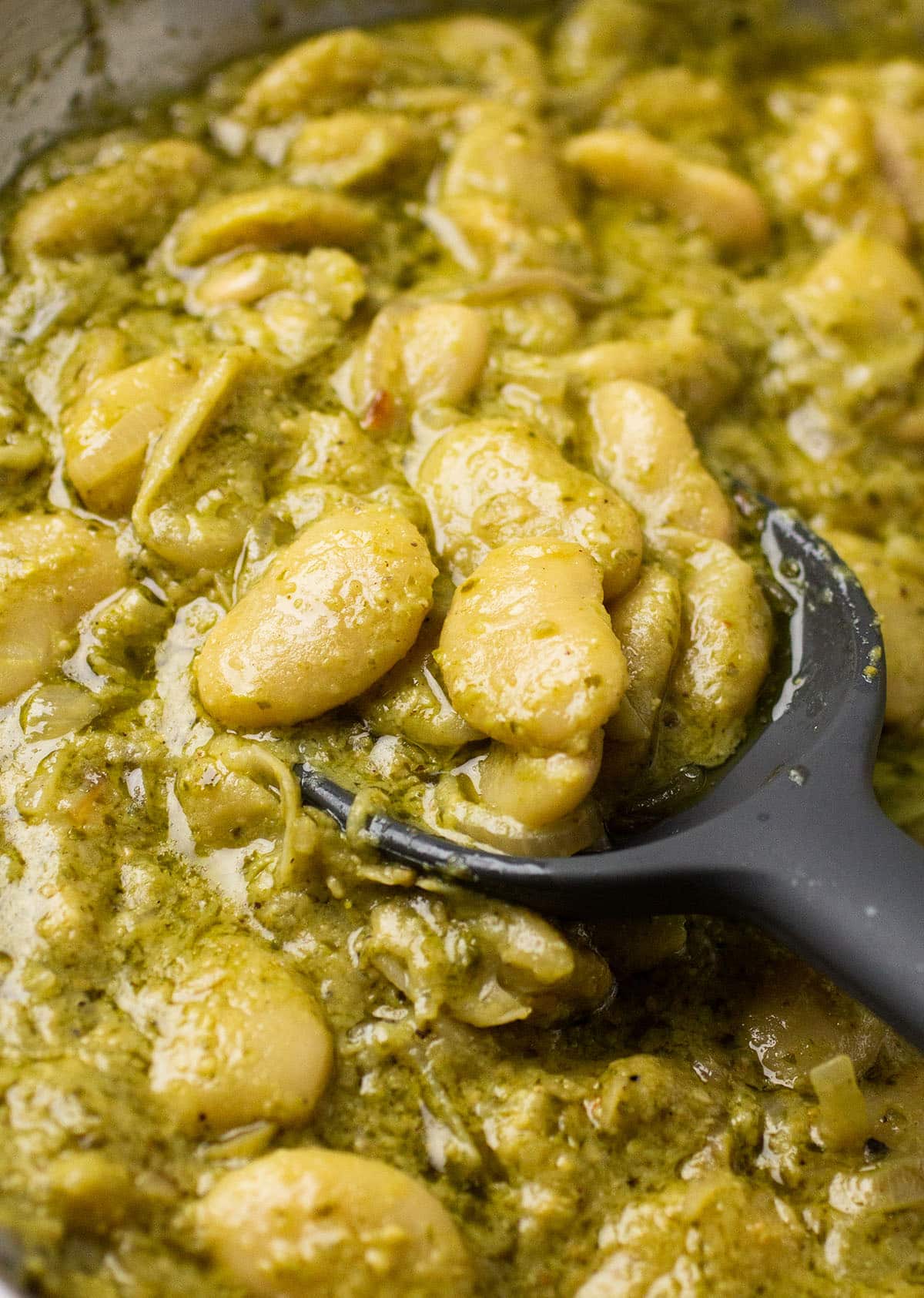 Black spatula stirring butter beans and pesto together.