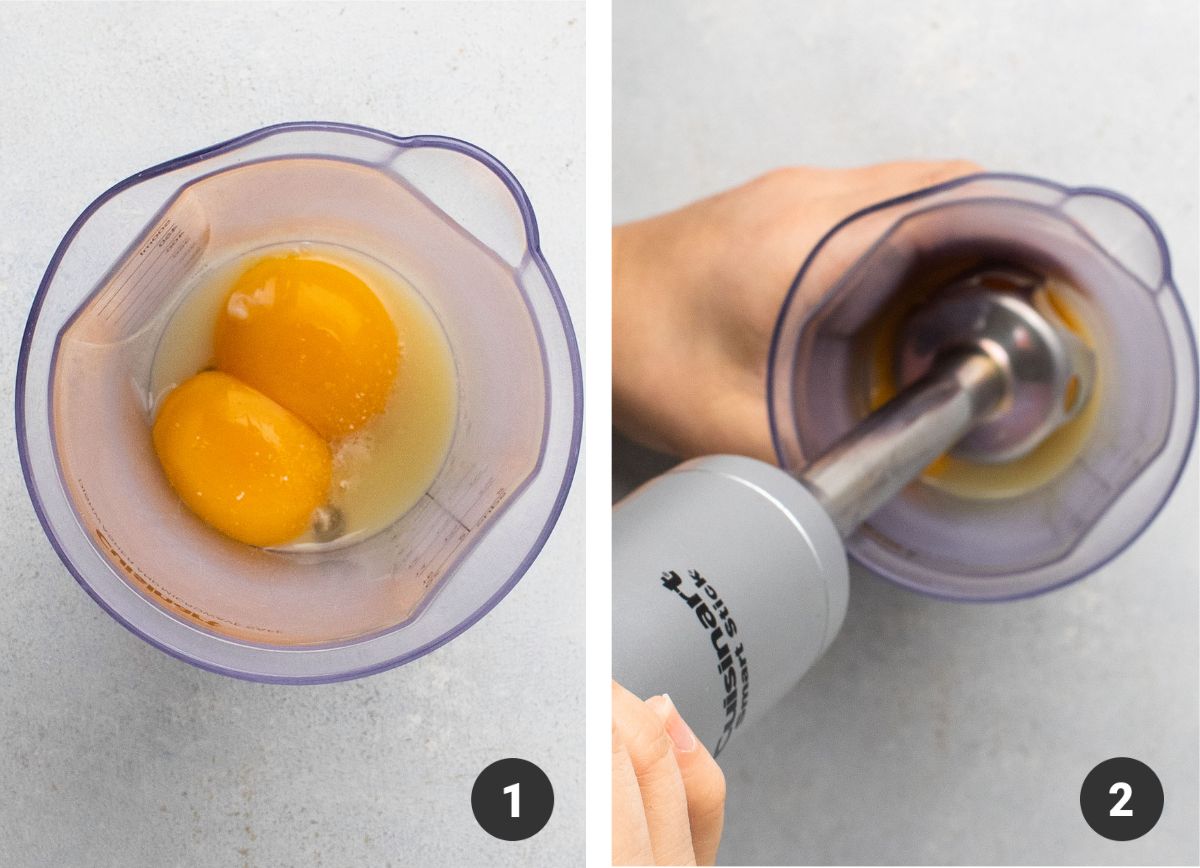 Blending egg yolks in a plastic cup with an immersion blender.