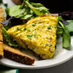 Slice of leek frittata on a white plate with a side salad.