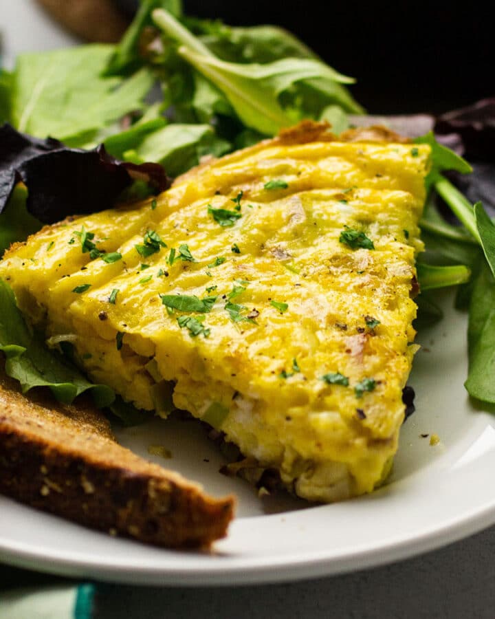 Slice of leek frittata on a white plate with a side salad.