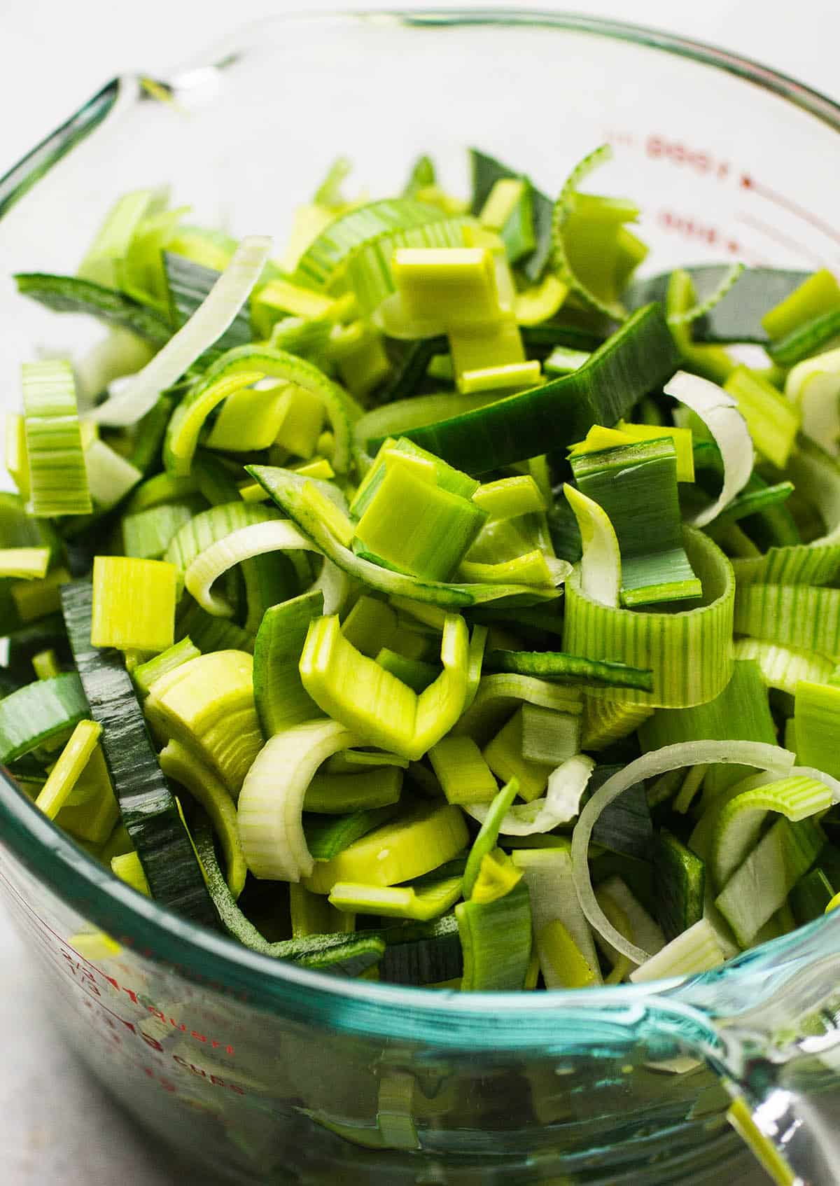 Sliced leeks in a large glass measuring cup.